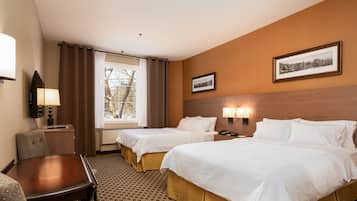 A hotel room with two beds, a desk, a chair, a lamp, and a window with curtains.