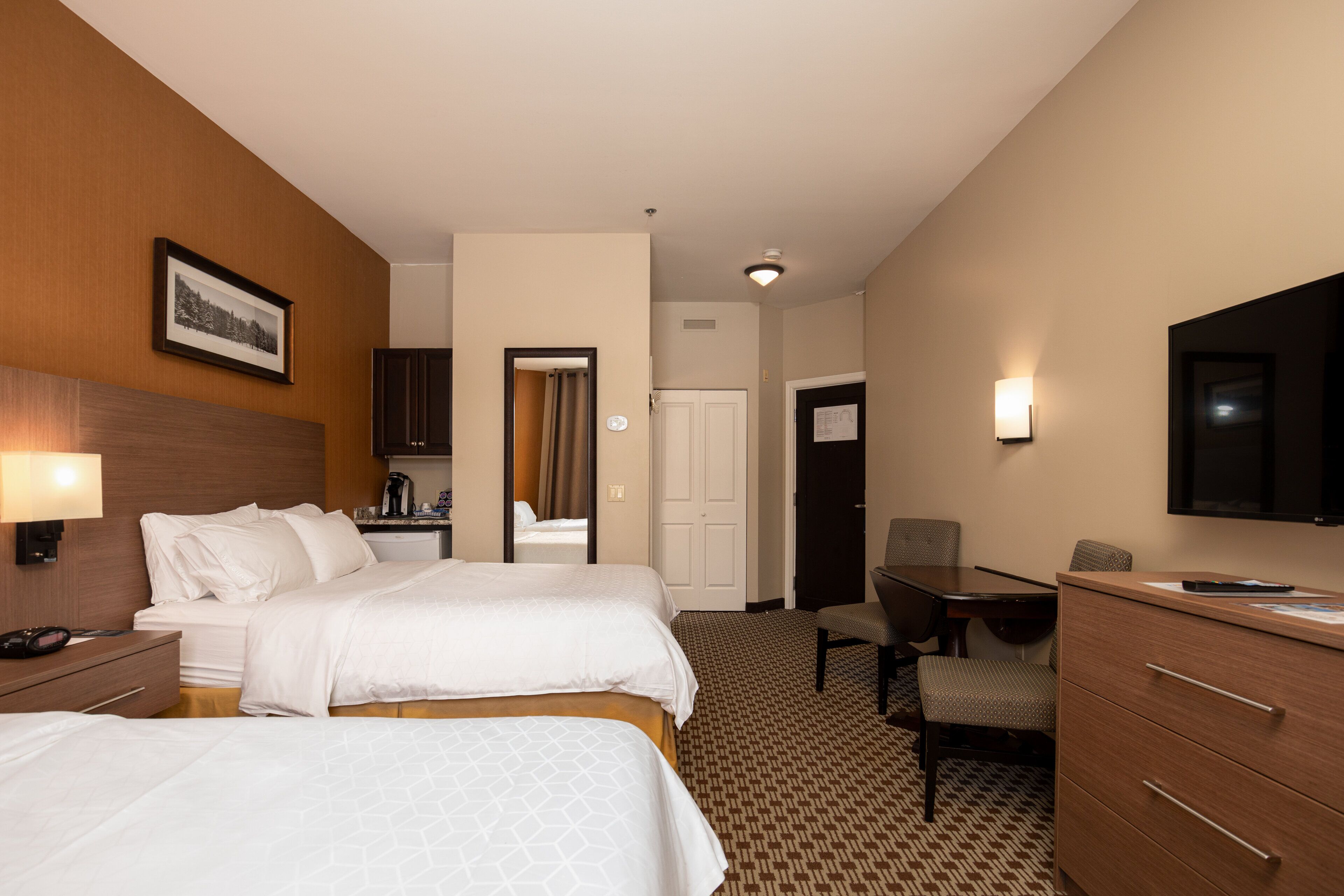 Habitación de hotel con dos camas, un escritorio, una silla, un televisor y un baño visible a través de una puerta abierta.