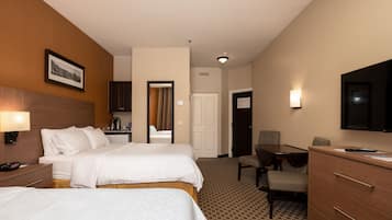 Habitación de hotel con dos camas, un escritorio, una silla, un televisor y un baño visible a través de una puerta abierta.