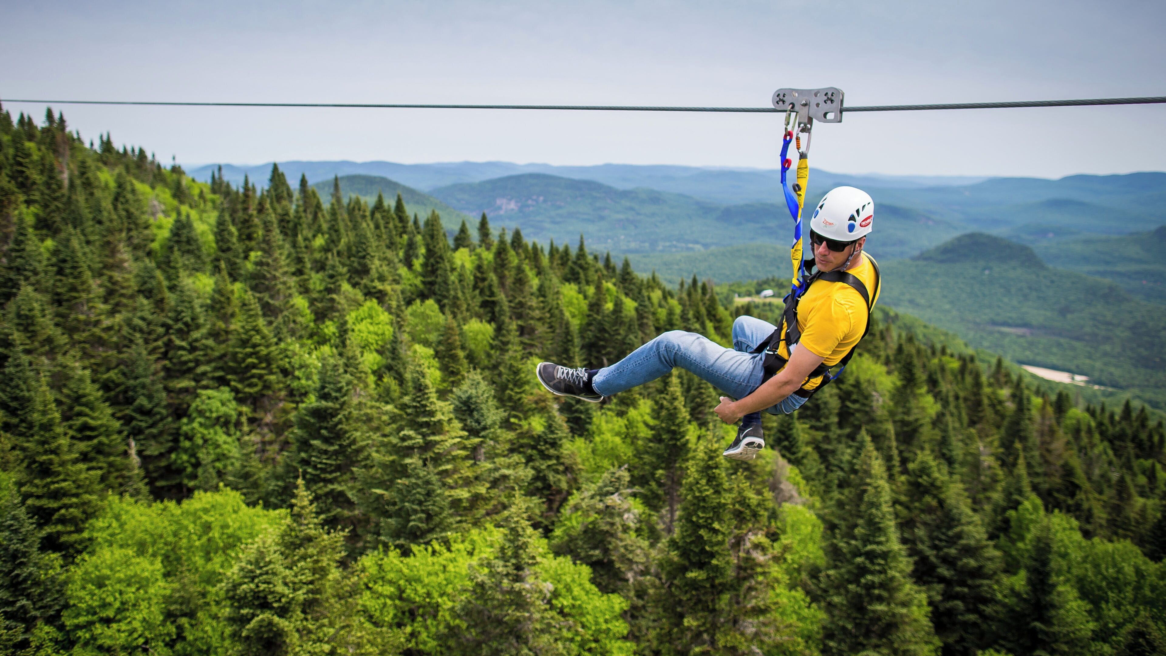 Eine Person saust an einer Zipline durch ein bewaldetes Gebiet mit freiem Blick auf die Landschaft.