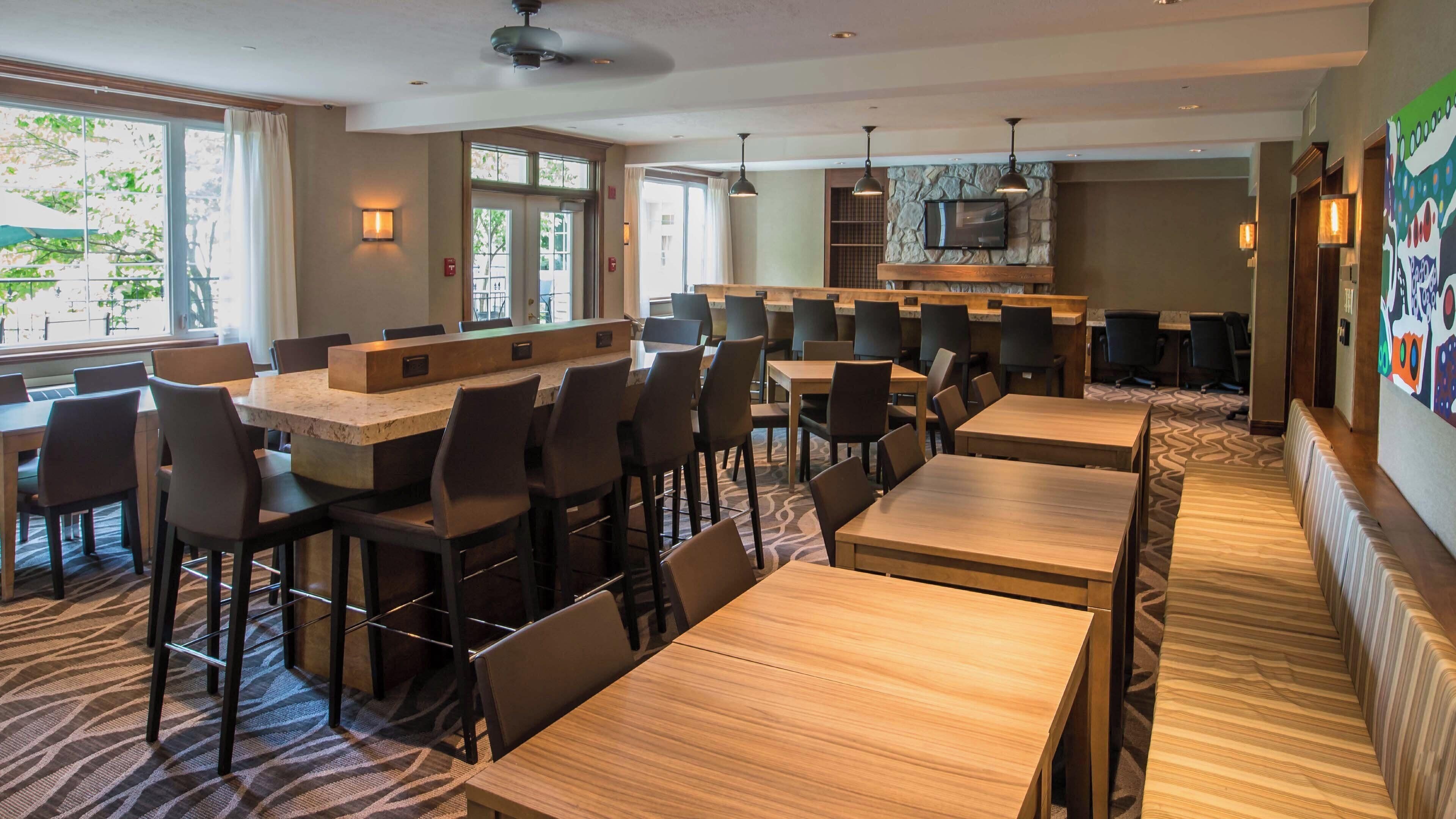 A restaurant with a long counter, multiple tables, and chairs. There is a stone wall with a TV, and the room has a ceiling fan.