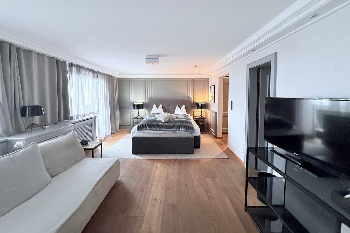 A modern hotel room with a large bed, a sofa, a TV, and a desk.