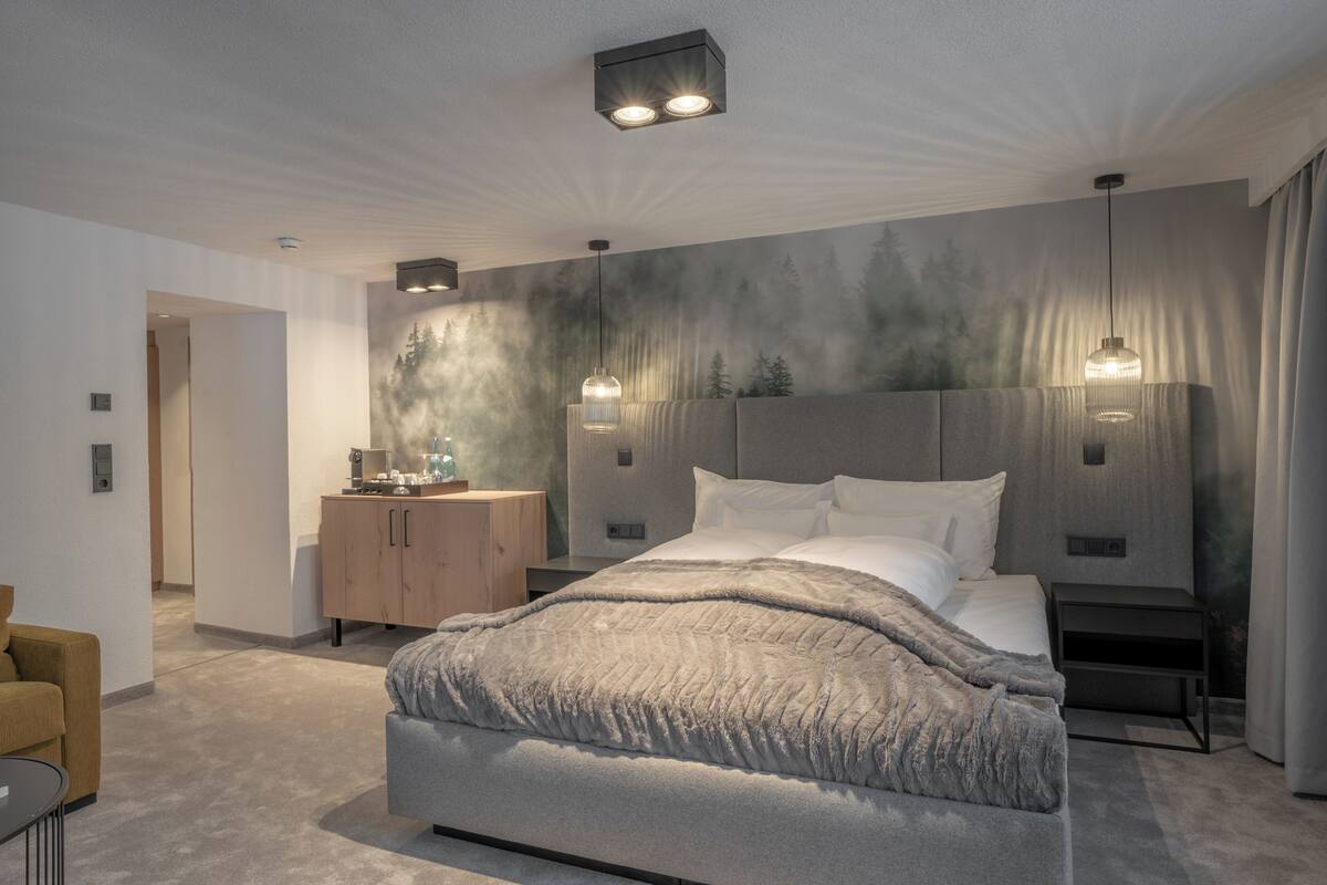A modern bedroom with a large bed, bedside tables, a wardrobe, and a wall mural.