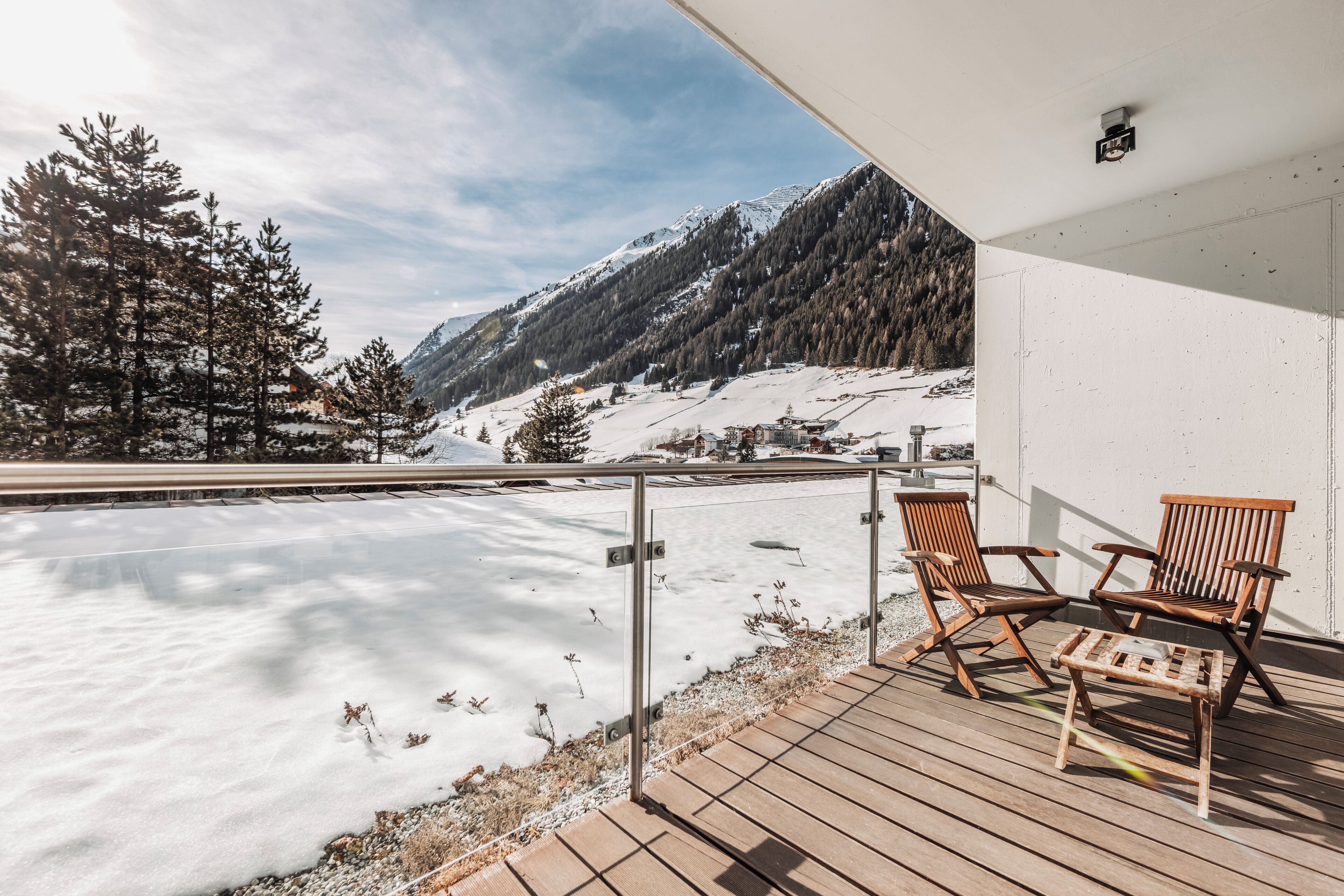 A wooden deck with two chairs, a snow-covered landscape, and a mountain in the background.