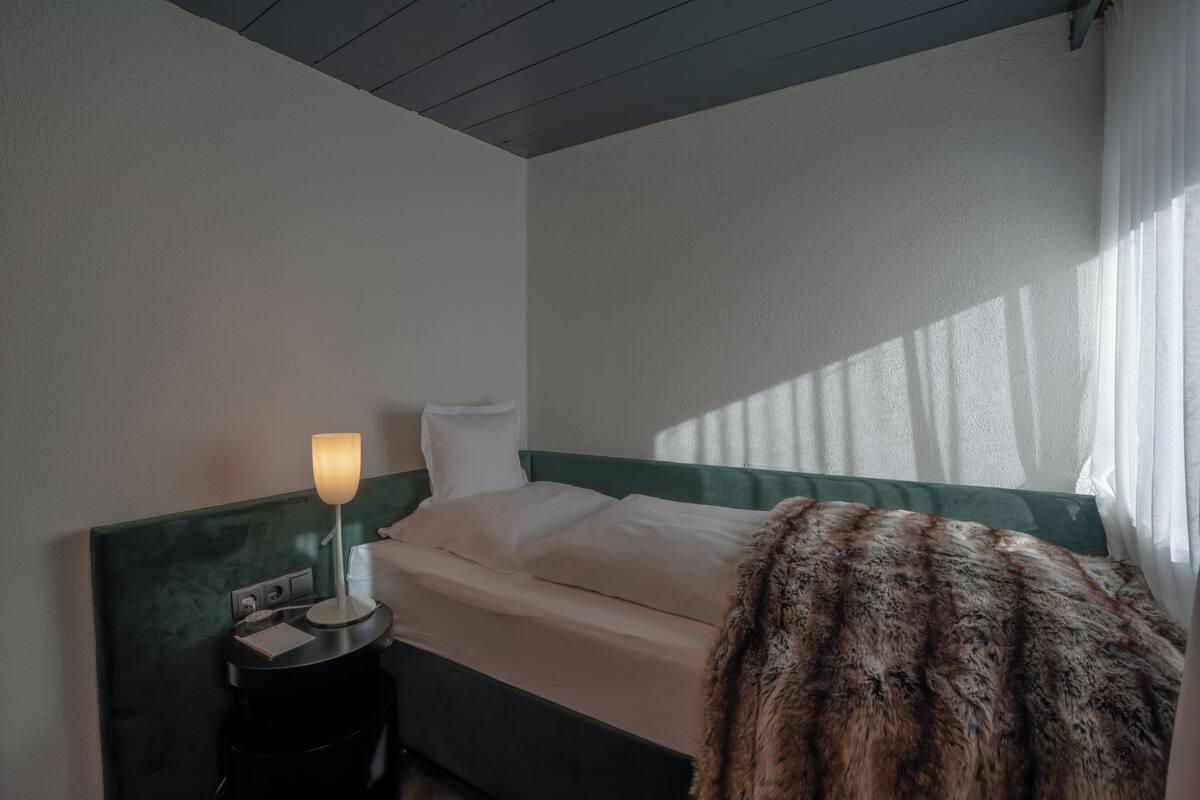 A hotel room with a bed, a nightstand with a lamp, and a fur throw on the bed.