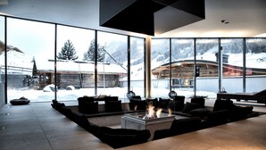 Un espacio interior moderno con chimenea, asientos y ventanas amplias con vistas a un paisaje nevado.