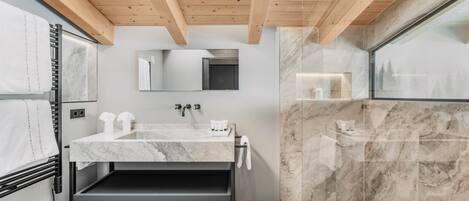 A modern bathroom with a marble sink, a mirror, and a shower area.