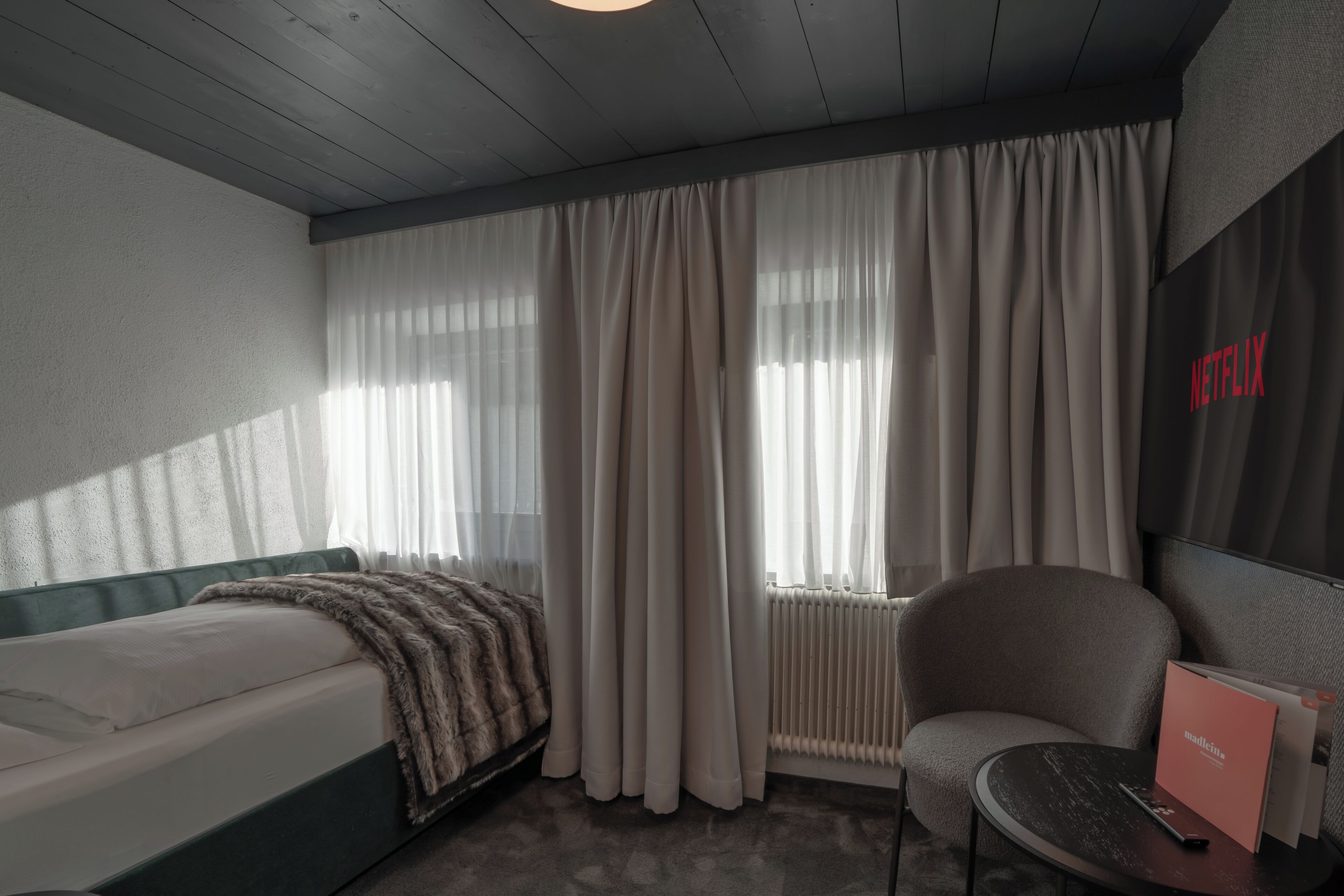 Una habitación de hotel con una cama, una silla, una mesa y un radiador.