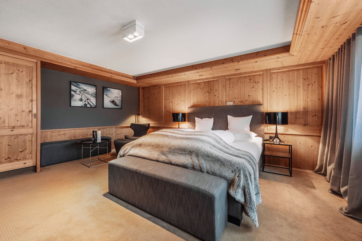 A bedroom with a bed, bedside tables, a bench, and wooden paneling.