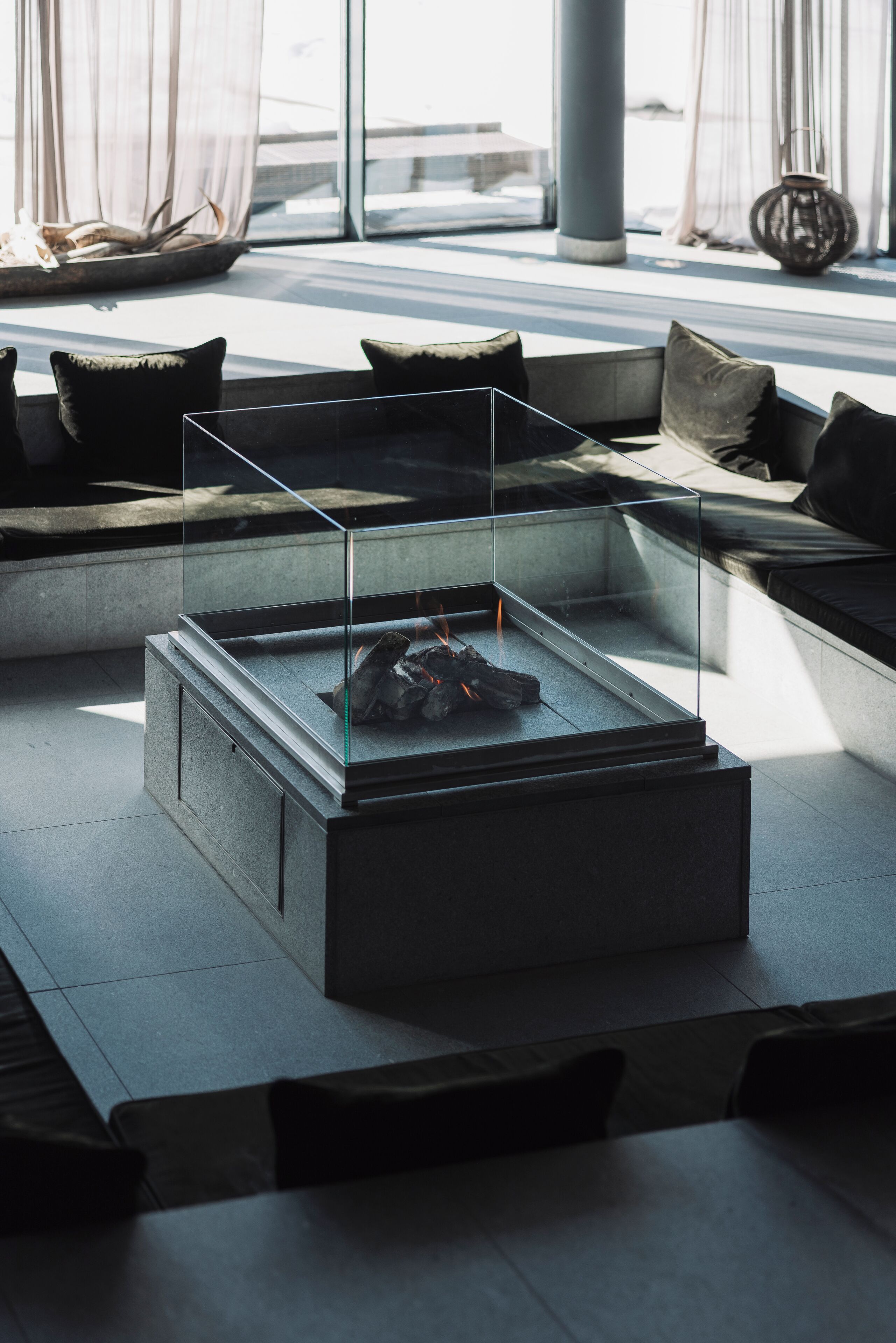 Un área lounge moderna con una mesa de centro de vidrio, asientos con cojines y un jarrón decorativo.