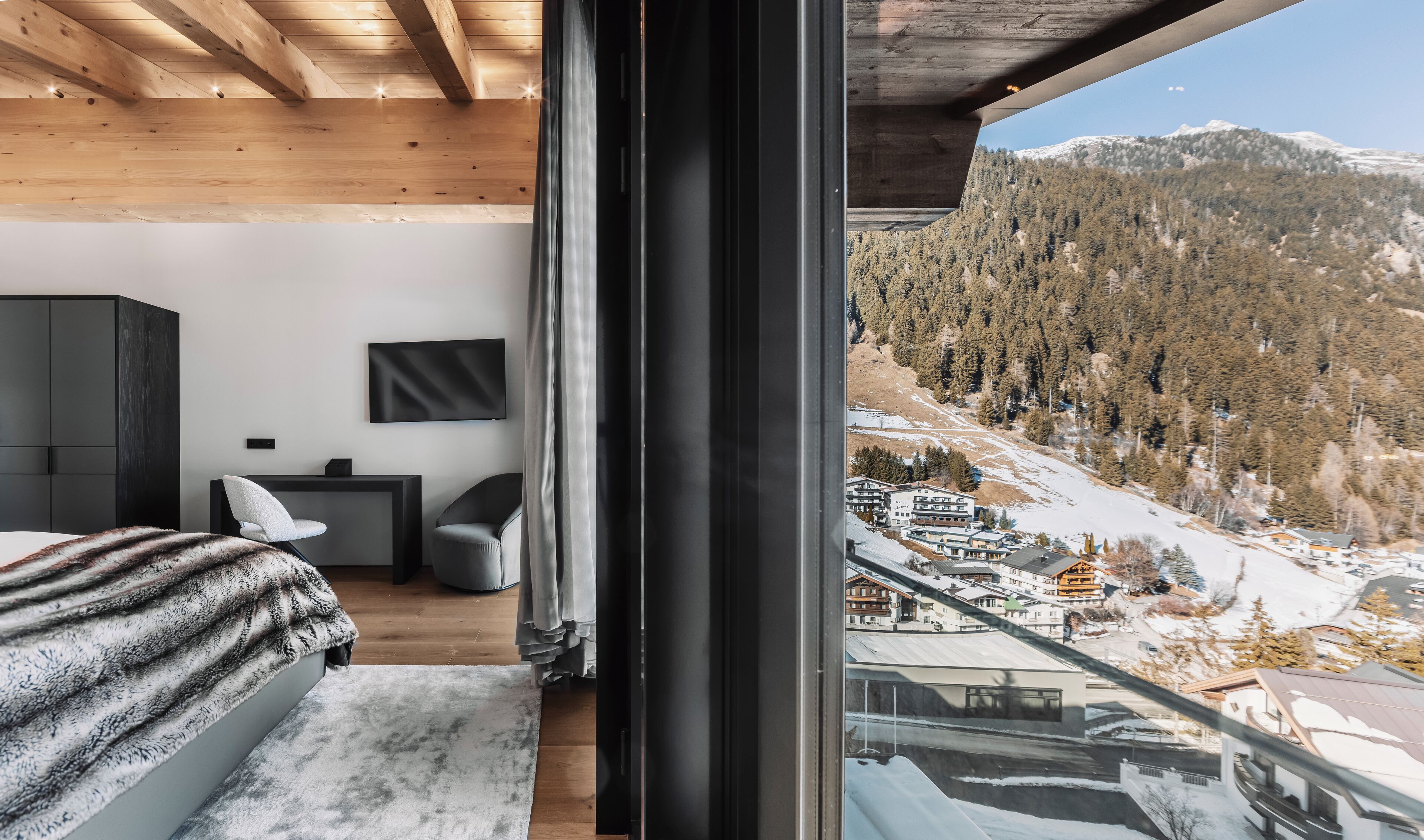 Une chambre moderne avec une grande fenêtre, un plafond en bois et une vue sur un paysage montagneux enneigé.