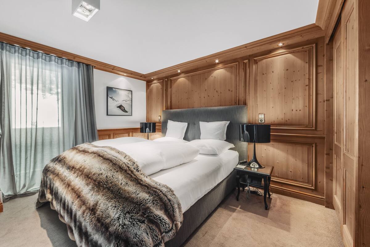 A hotel room with a large bed, wooden paneling, a nightstand with a lamp, and a painting on the wall.