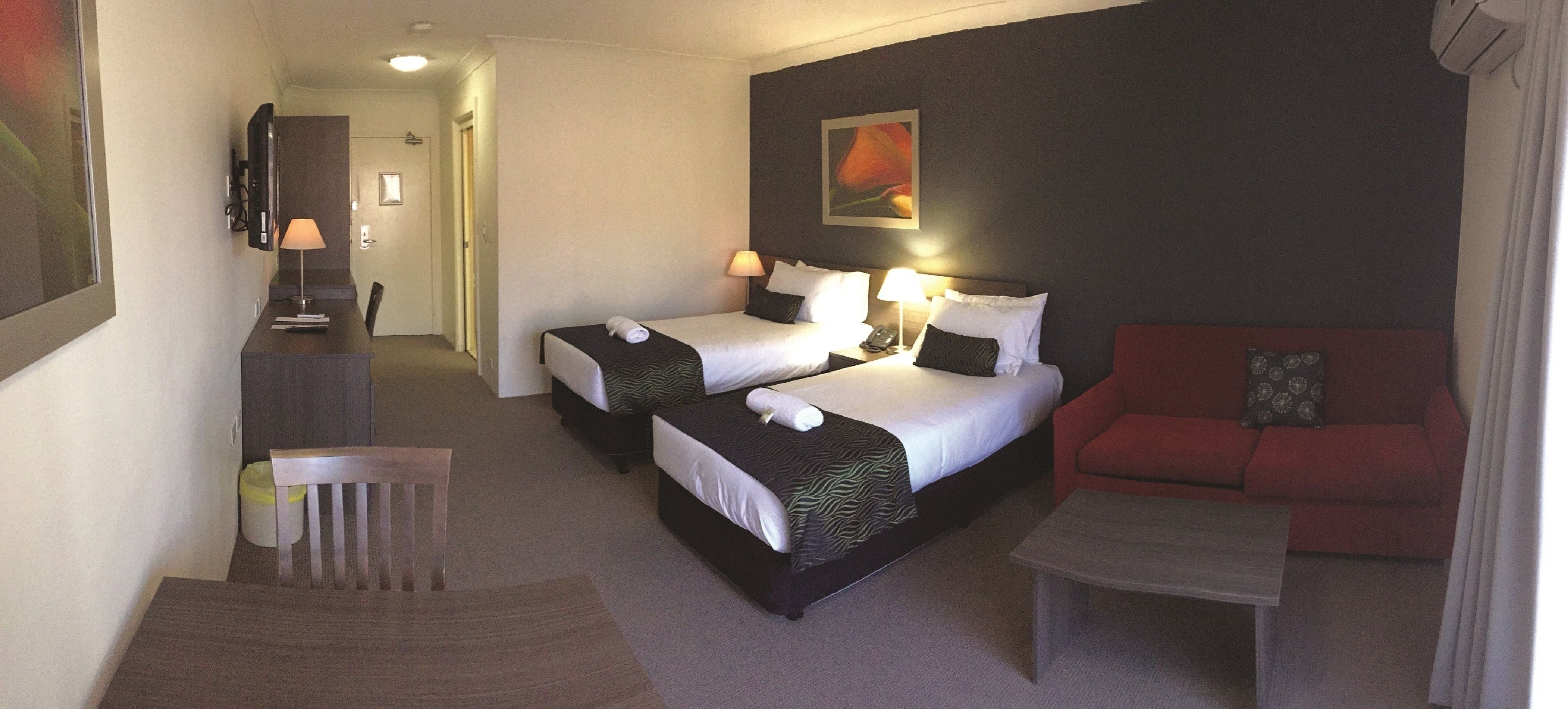 Habitación de hotel con dos camas, un sofá rojo, una mesita y un televisor sobre un mueble.