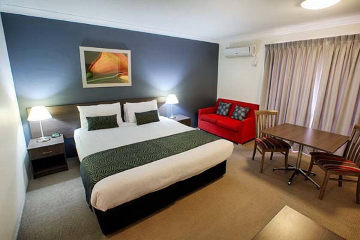 Ein Hotelzimmer mit einem großen Bett, einem roten Sofa, einem Esstisch mit Stühlen und einem Bild an der Wand.