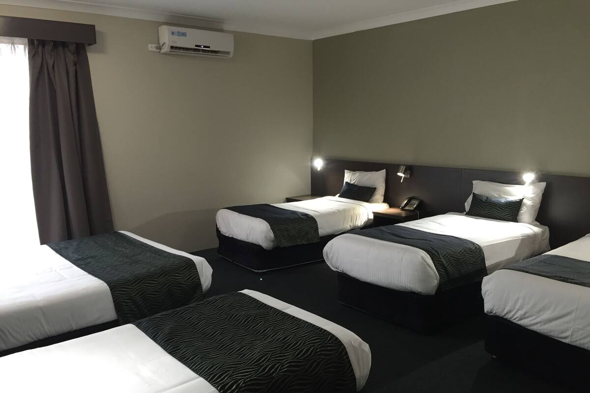 Ein Hotelzimmer mit vier Einzelbetten, einer Wandklimaanlage und einem Nachttischtelefon.