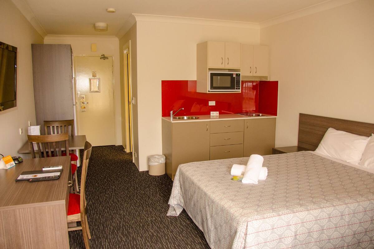 Ein Hotelzimmer mit Bett, Schreibtisch, Stuhl, Mikrowelle und einer kleinen Küchenzeile.