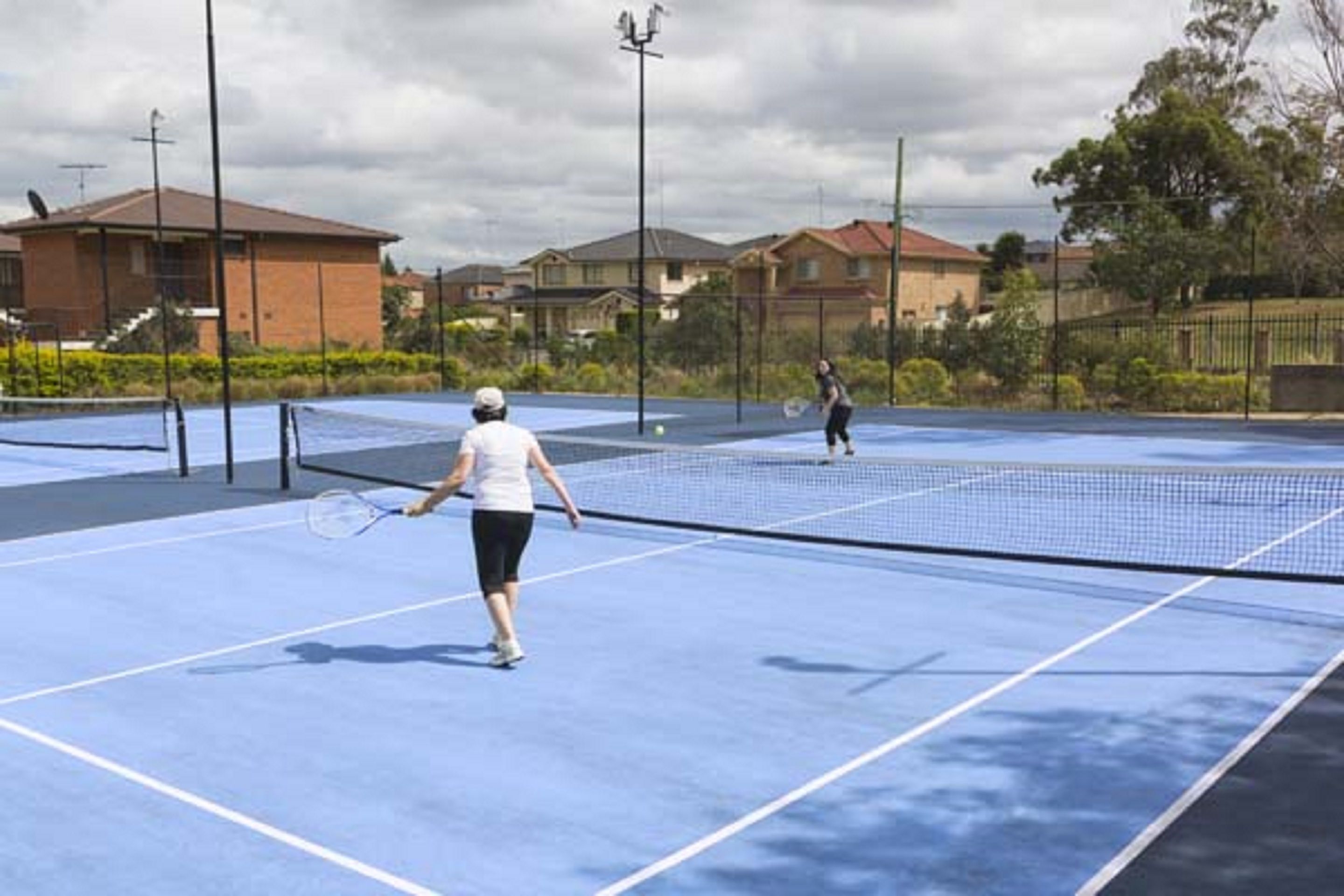 Een tennisbaan met een net, omringd door huizen en groen.
