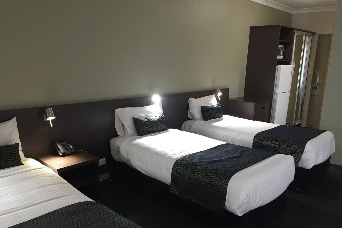 Ein Hotelzimmer mit zwei Betten, einem Nachttisch mit Telefon, einem Schrank und einer Mikrowelle.
