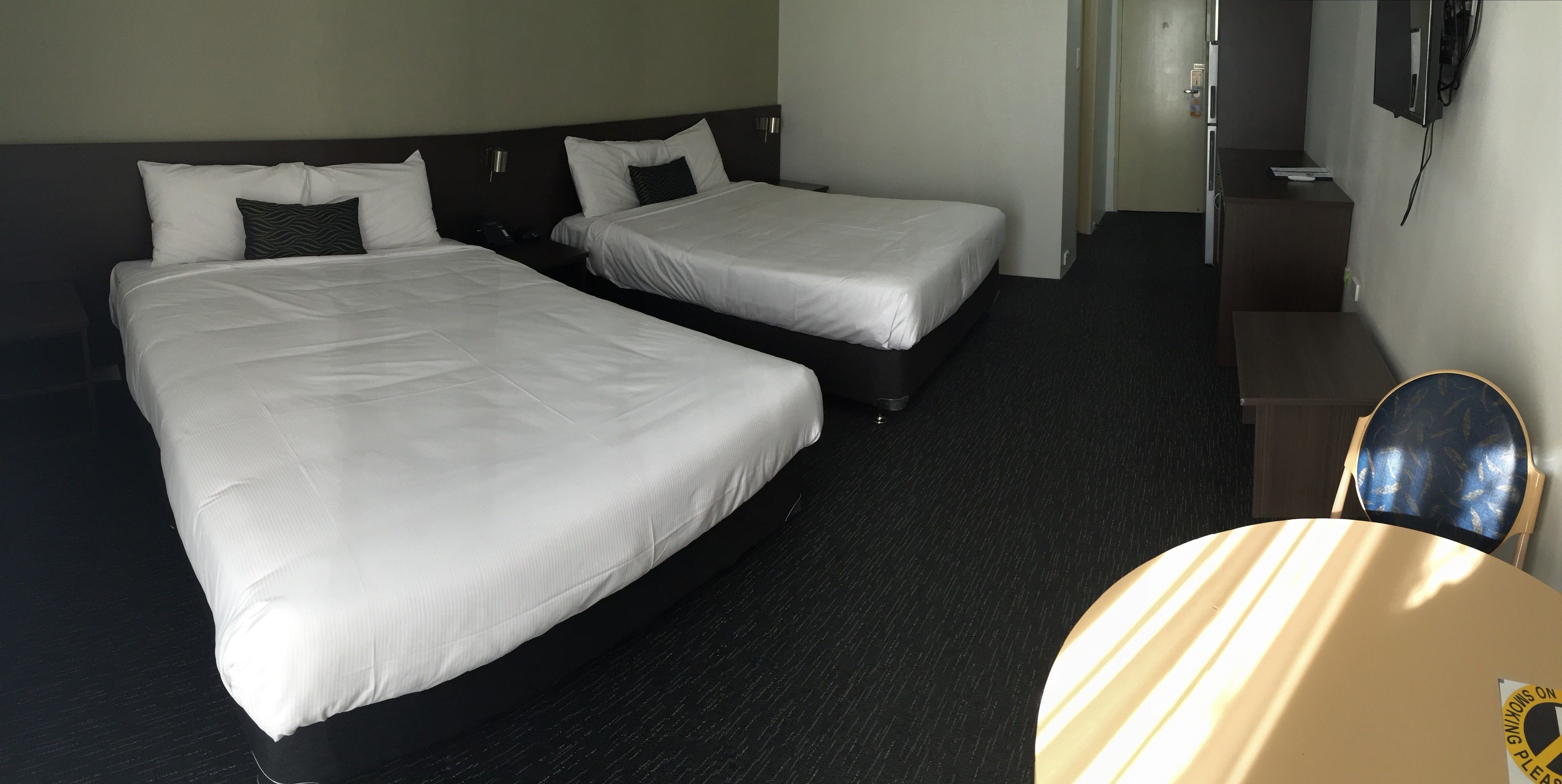 A hotel room with two single beds, a small desk, a chair, and a television mounted on the wall.