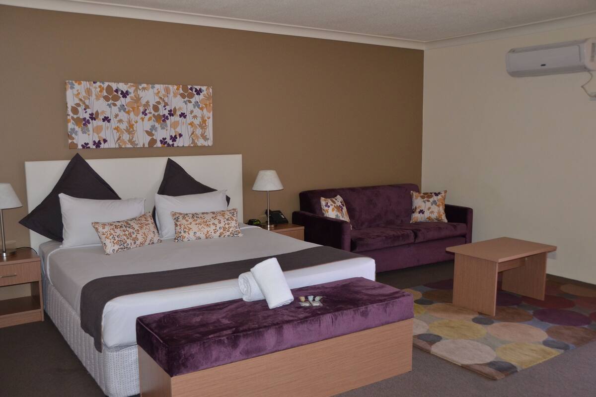 Ein Hotelzimmer mit einem großen Bett, einem violetten Sofa, einem kleinen Tisch und einer dekorativen Wanddekoration.
