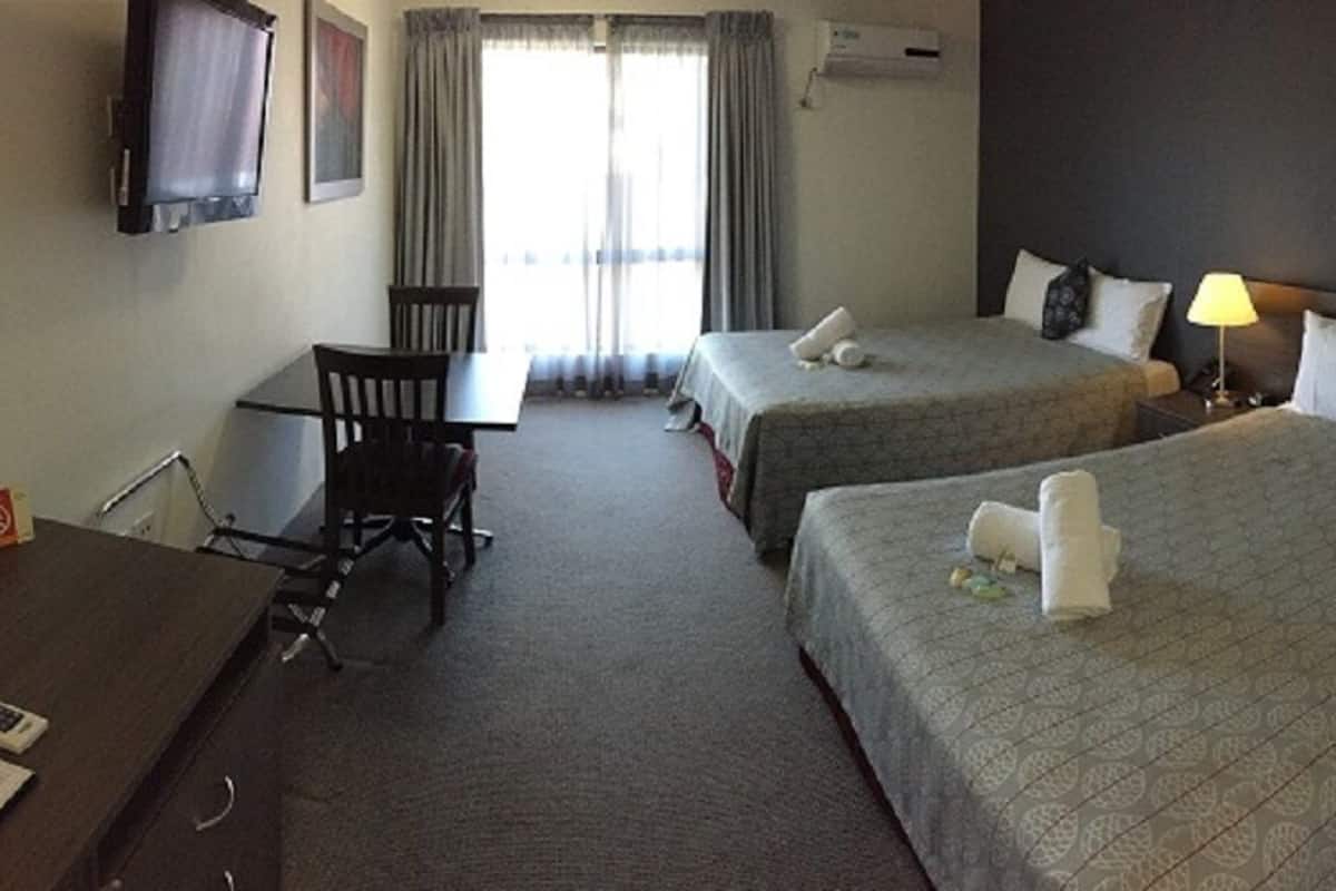 Ein Hotelzimmer mit zwei Betten, einem Schreibtisch, einem Sessel und einem Fernseher.