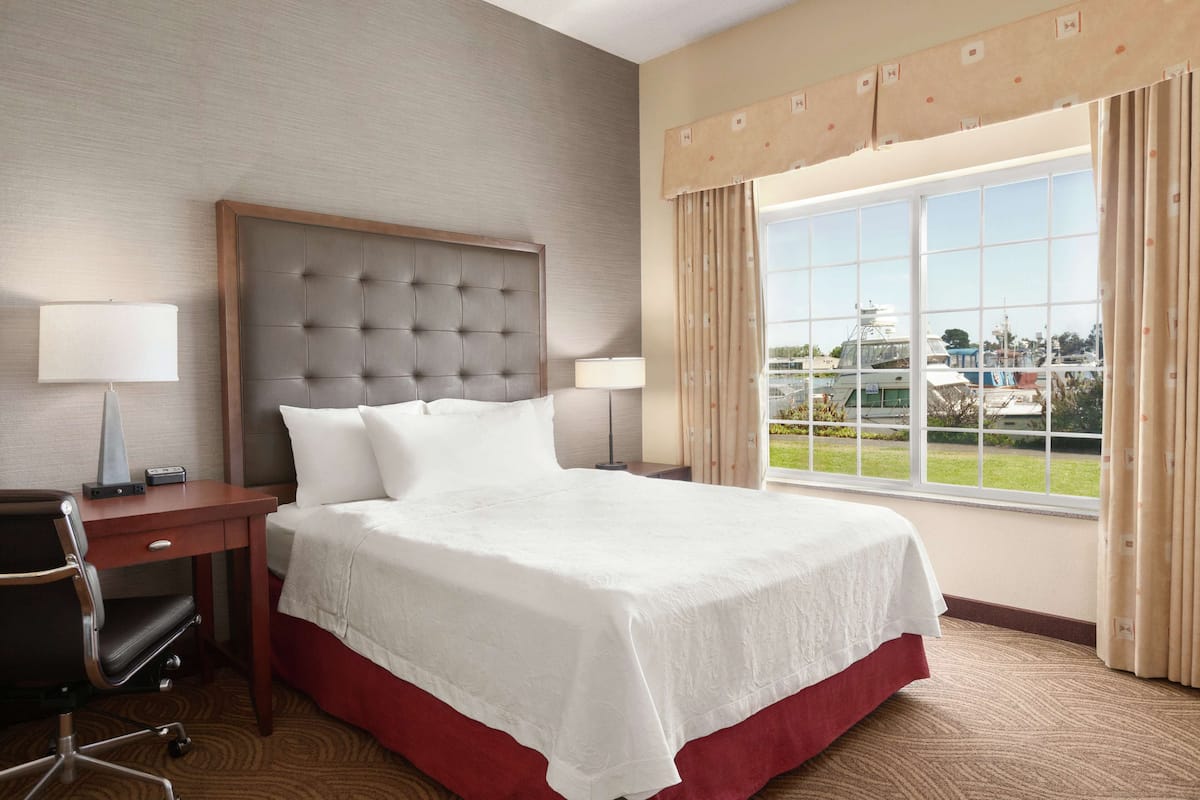 Ein Hotelzimmer mit einem großen Bett, einem Schreibtisch und einem Stuhl. Ein Fenster bietet einen Blick nach draußen.