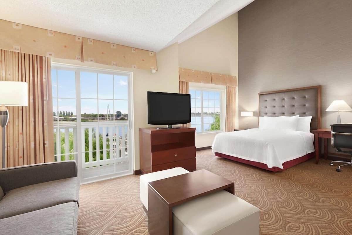 Ein Hotelzimmer mit Bett, Fernseher, Schreibtisch, Stuhl und Blick ins Freie.