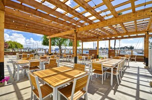 An outdoor patio with wooden tables and chairs, a pergola with string lights, and a view of the marina. - Homewood Suites by Hilton Oakland-Waterfront (Oakland)
