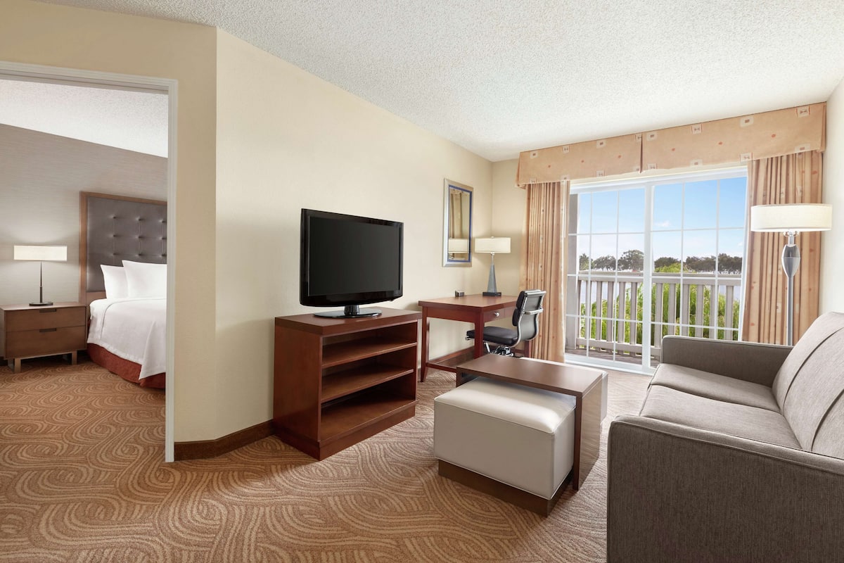 Ein Hotelzimmer mit Bett, Fernseher, Schreibtisch, Stuhl, Sofa und einem Balkon mit Aussicht.