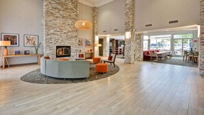 A spacious lobby with a stone accent wall, a fireplace, and a seating area with orange ottomans. - Homewood Suites by Hilton Oakland-Waterfront (Oakland)