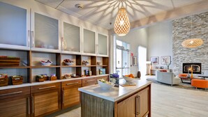 A modern kitchen with wooden cabinets, a central island, and a stone accent wall. - Homewood Suites by Hilton Oakland-Waterfront (Oakland)