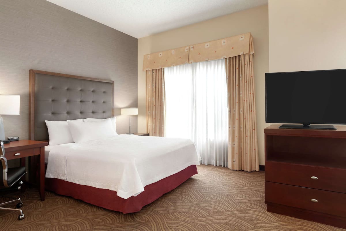 Ein Hotelzimmer mit einem großen Bett, einem Nachttisch aus Holz, einem Fernseher und einem Schreibtisch mit Stuhl.