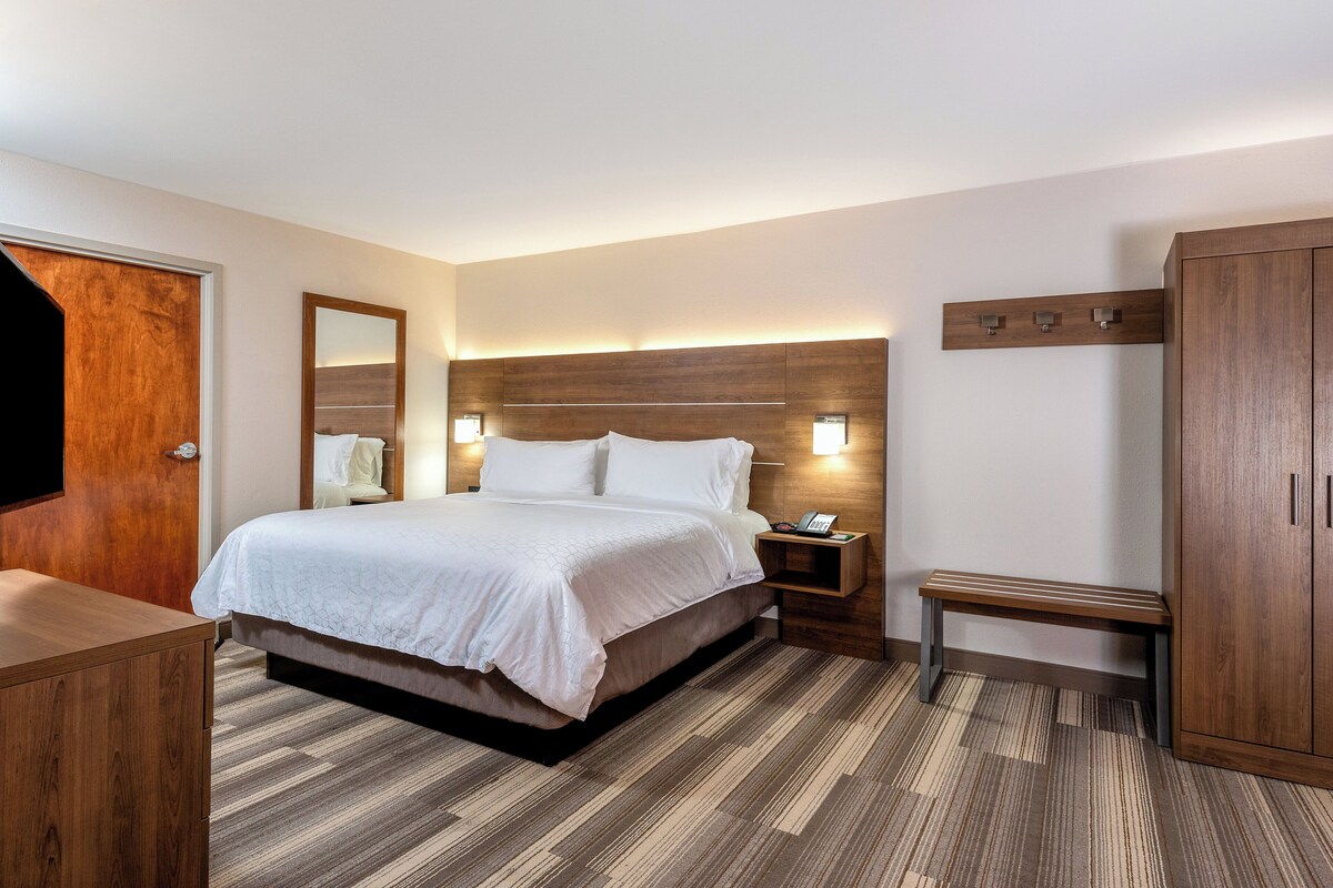 A hotel room with a bed, bedside table, nightstand, bench, wardrobe, and a wooden door.