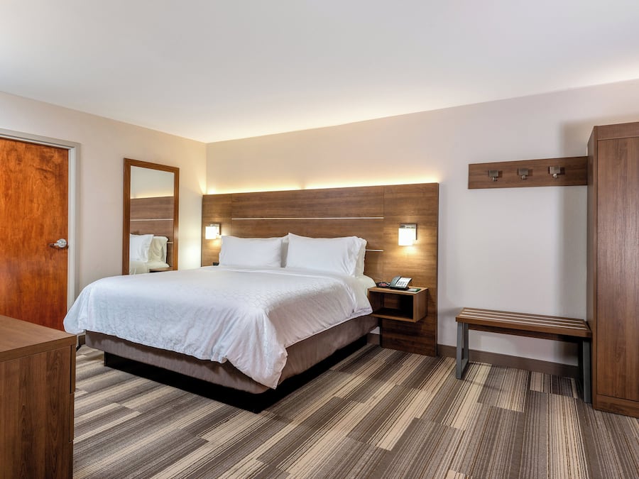 Habitación de hotel con cama, mesita de noche, banco, armario y una puerta de madera.