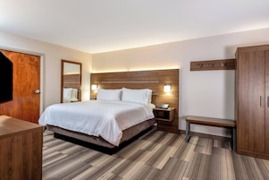 Habitación de hotel con cama, mesita de noche, banco, armario y una puerta de madera.