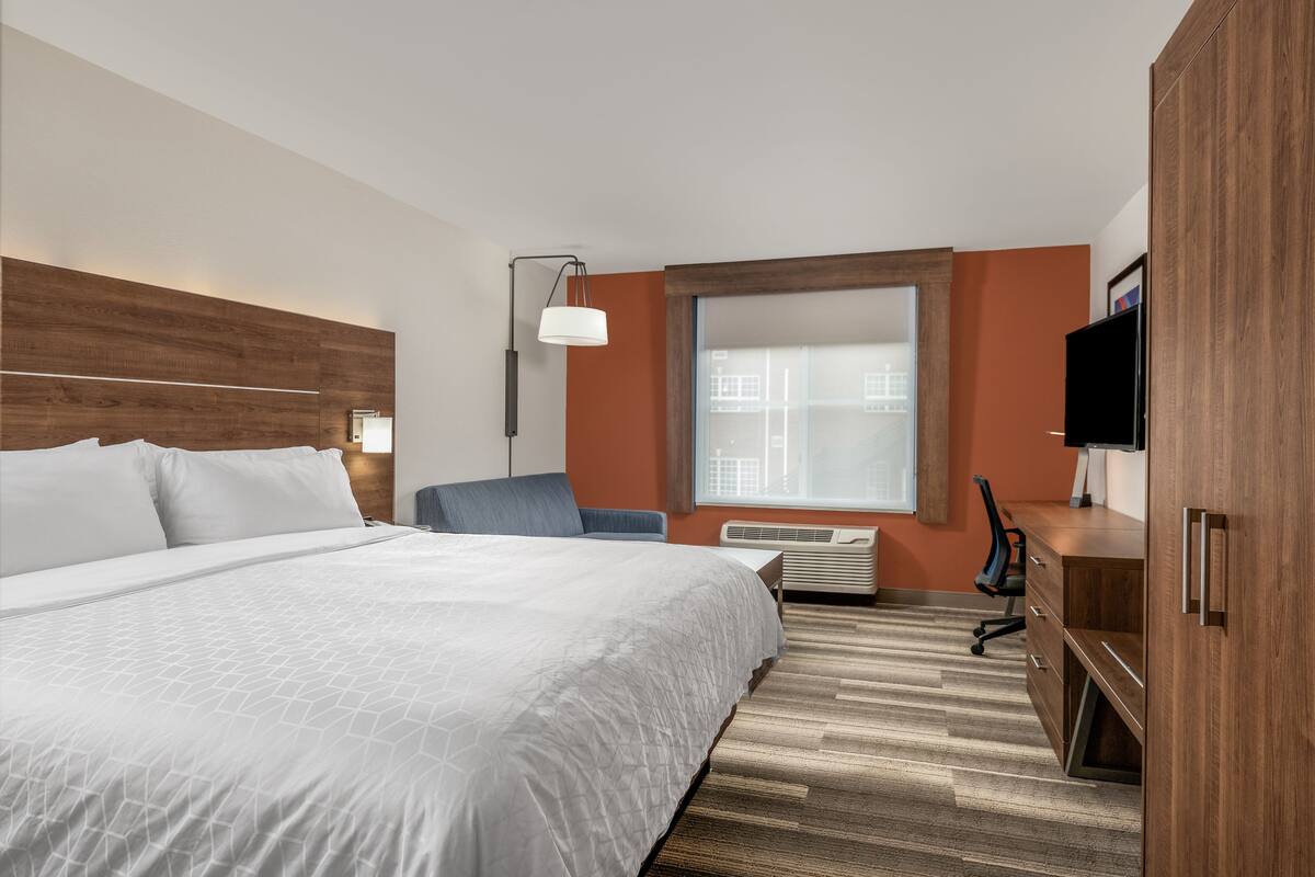 A hotel room with a large bed, a desk, a chair, and a TV.