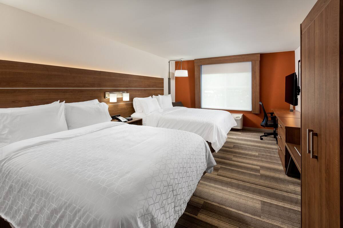 A hotel room with two beds, a desk, a chair, a TV, and a large window.