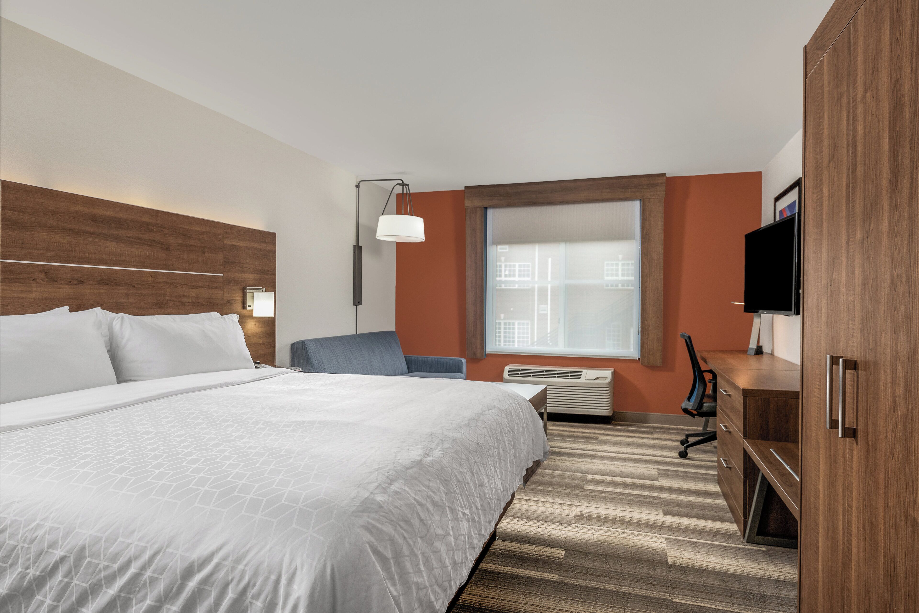 Una habitación de hotel con una cama grande, un escritorio, una silla, un televisor y una ventana con vistas a la ciudad.