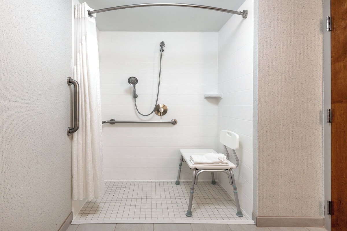 A shower area with a grab bar, a bench, and a towel rack.