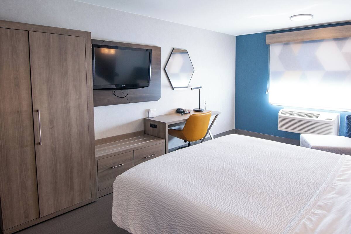 Habitación de hotel con cama, un escritorio con silla, un televisor en la pared y un equipo de aire acondicionado.