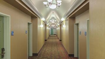 A hotel hallway with carpeted floors, doors with room numbers, and a chandelier.
