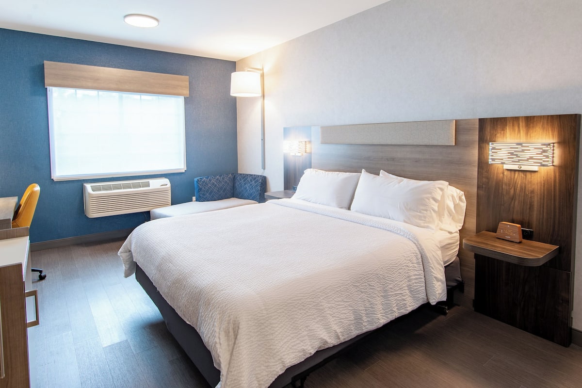 Una habitación de hotel moderna con una cama grande, mesitas de noche, un escritorio y una ventana con persianas.