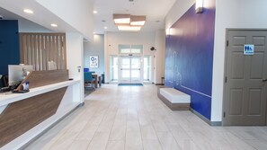 A hotel reception area with a reception desk, a seating area, and a blue wall with a cityscape mural.