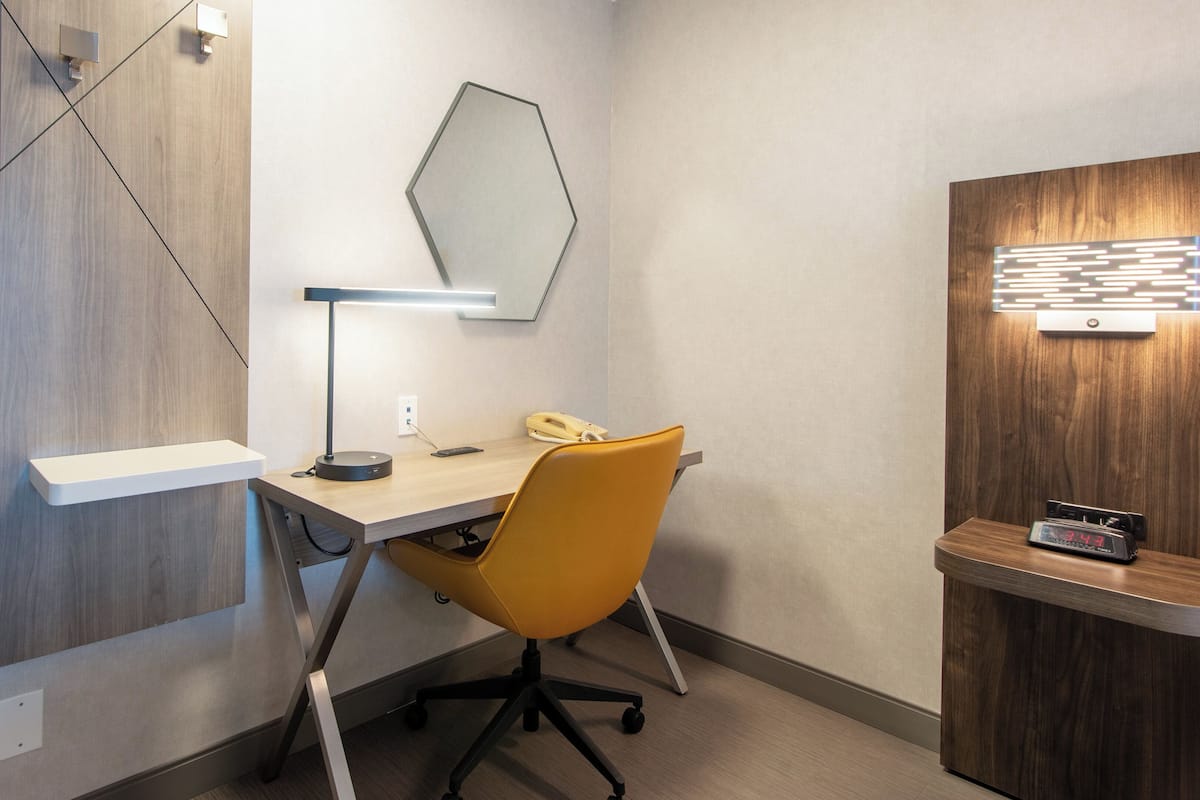 Un espacio de oficina moderno con escritorio, silla, lámpara, teléfono y reloj.