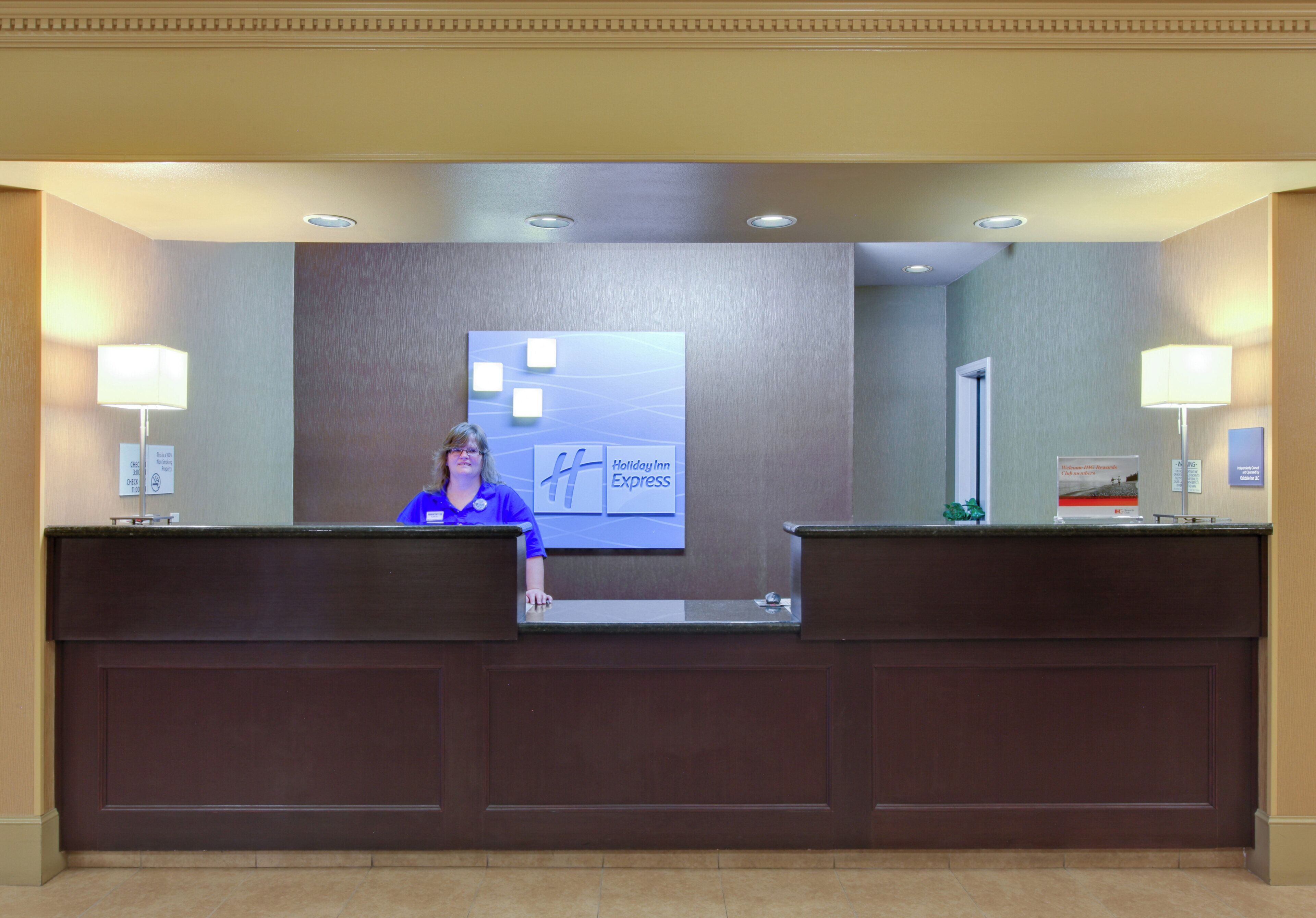 A hotel reception desk with a Holiday Inn Express sign, a nameplate, and a no-smoking sign.