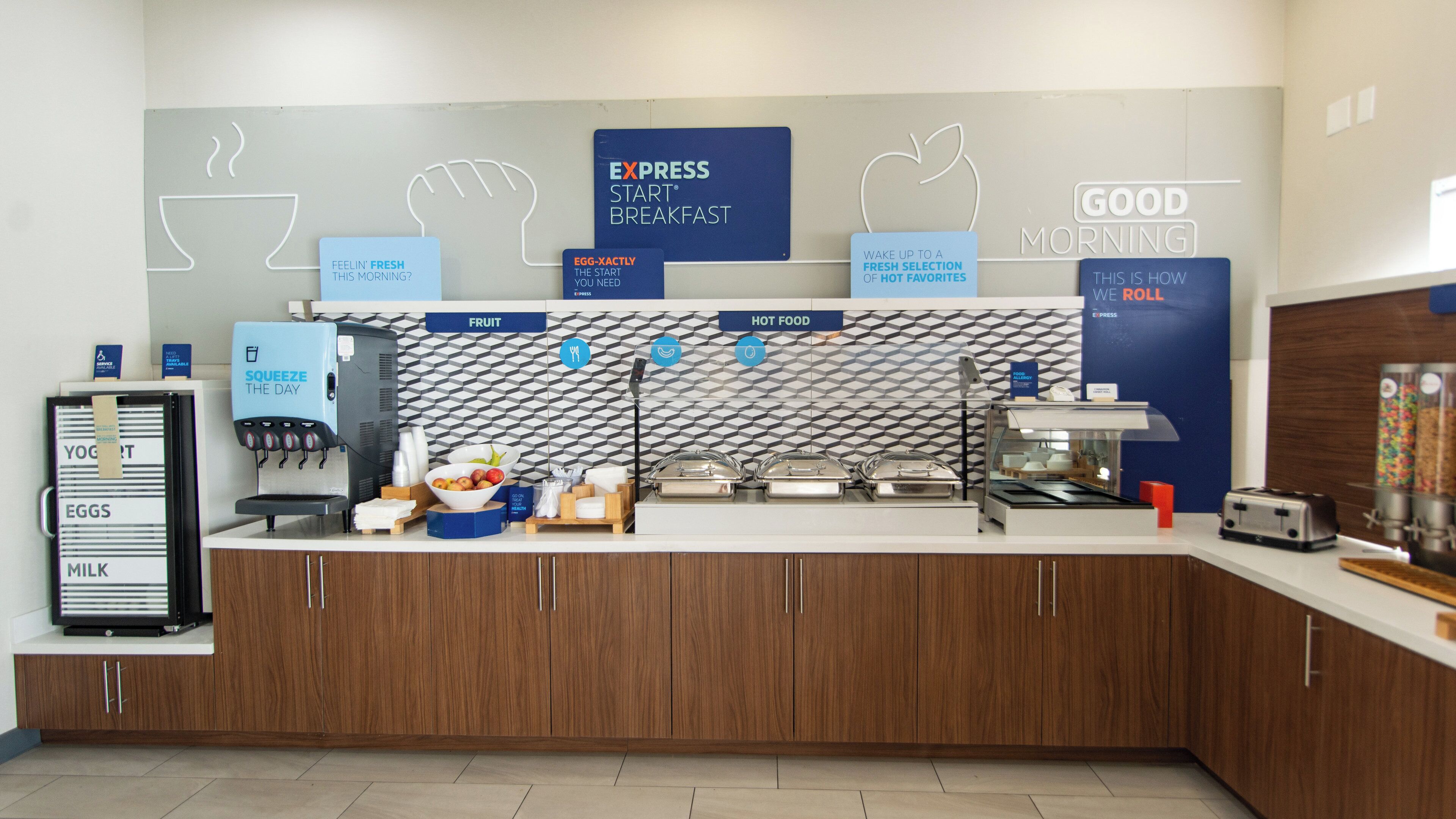 A breakfast station with labeled sections for eggs, milk, fruit, and hot food, including a coffee machine and a toaster.
