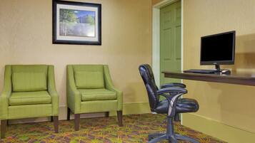 A room with two green armchairs, a black office chair, a desk with a computer monitor, and a framed picture on the wall.