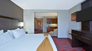 A hotel room with a large bed, a TV, a desk, and a kitchenette.