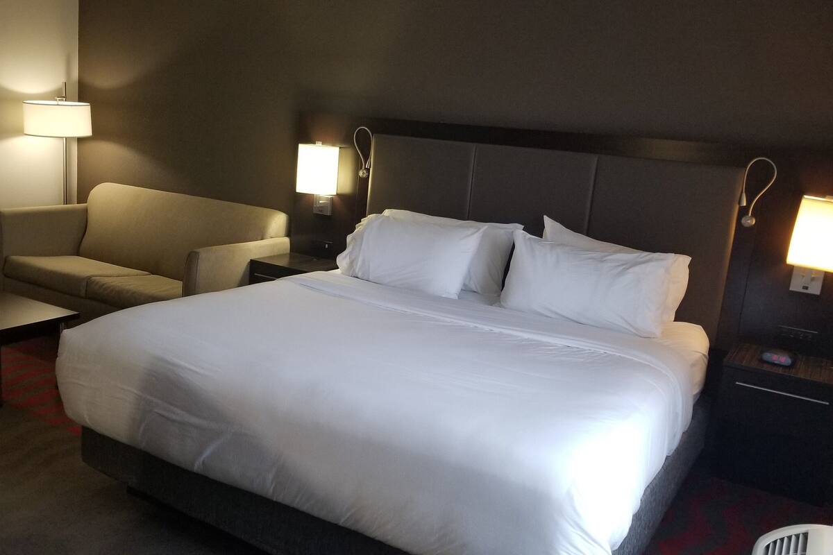 A hotel room with a large bed, a chair, a desk, and two bedside lamps.