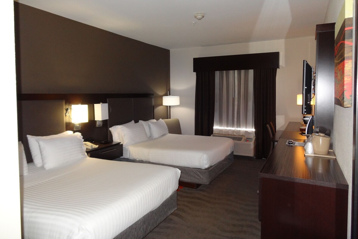 A hotel room with two beds, a desk, a chair, a TV, and a window with curtains.